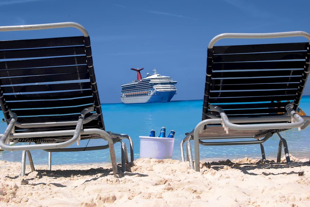Two empty beach chairs facing a cruise ship offshore